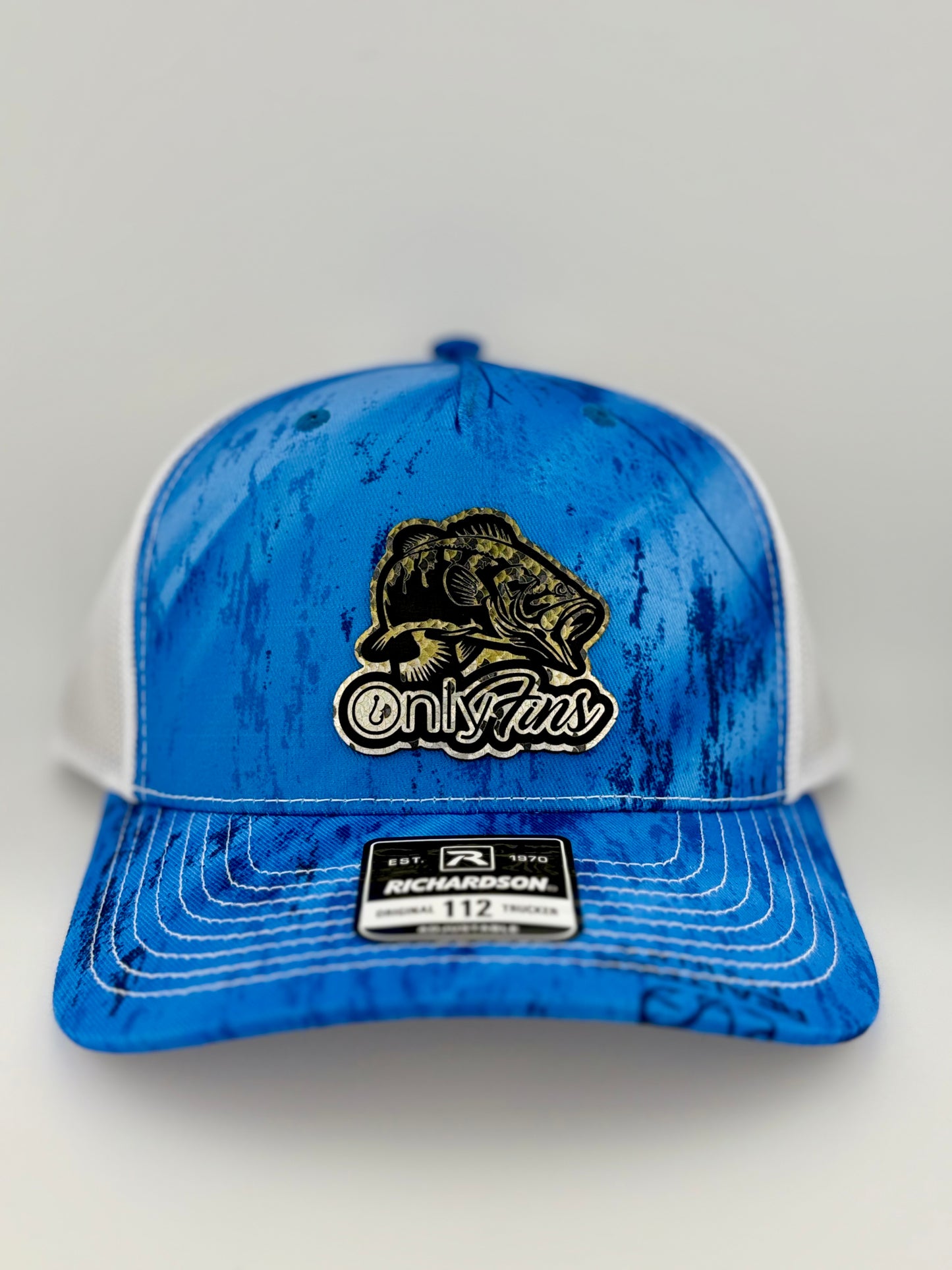 A blue and white Richardson 112 trucker hat with a water-textured pattern and a black and gold patch featuring a largemouth bass and the phrase "OnlyFins." The front panel is structured with a white mesh back.