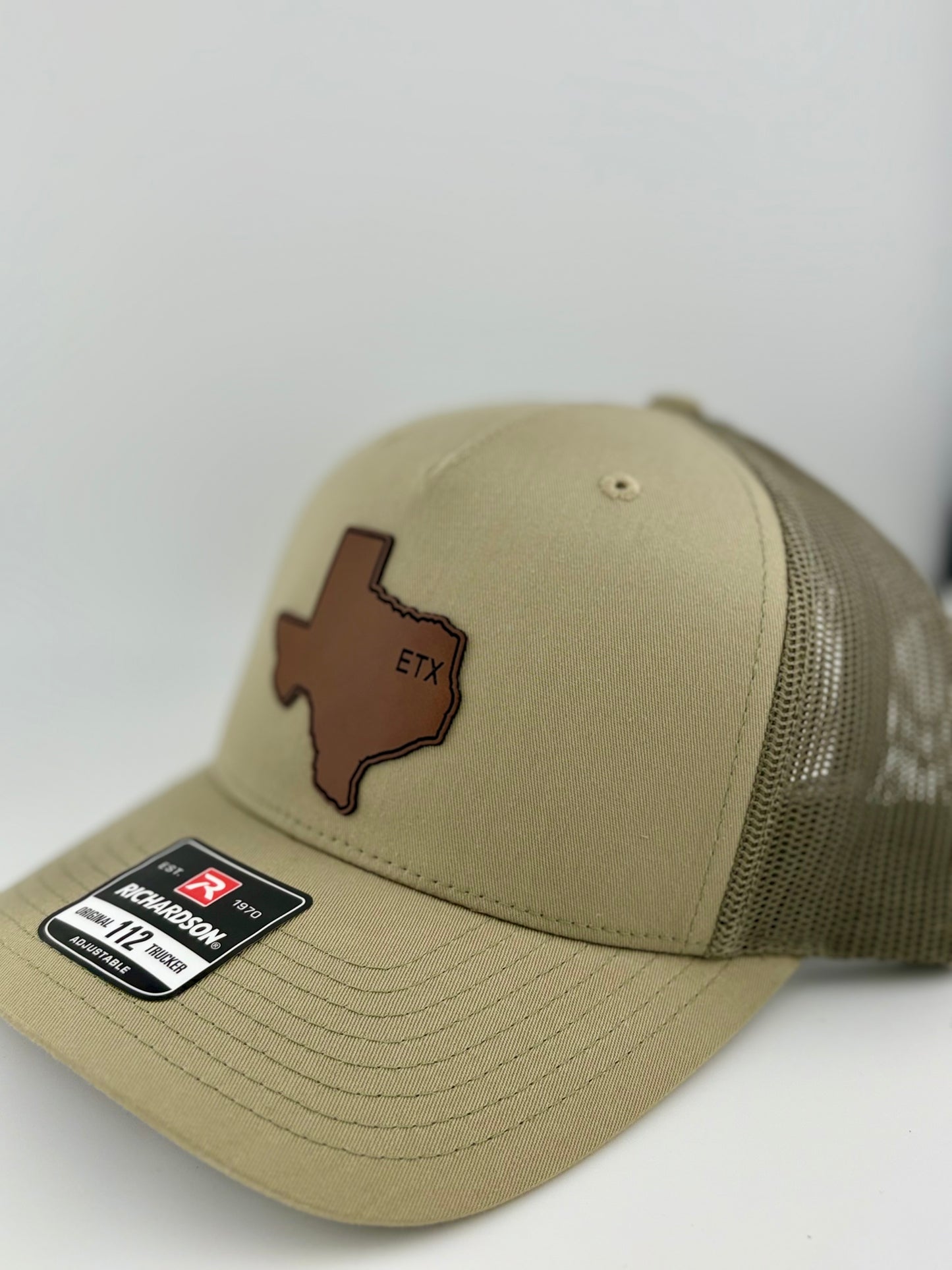 "Side view of a khaki trucker hat with a matching mesh back and structured front panel. The brown Texas-shaped patch with the embossed 'ETX' stands out, giving a rustic and regional aesthetic. A Richardson 112 label is visible on the brim."