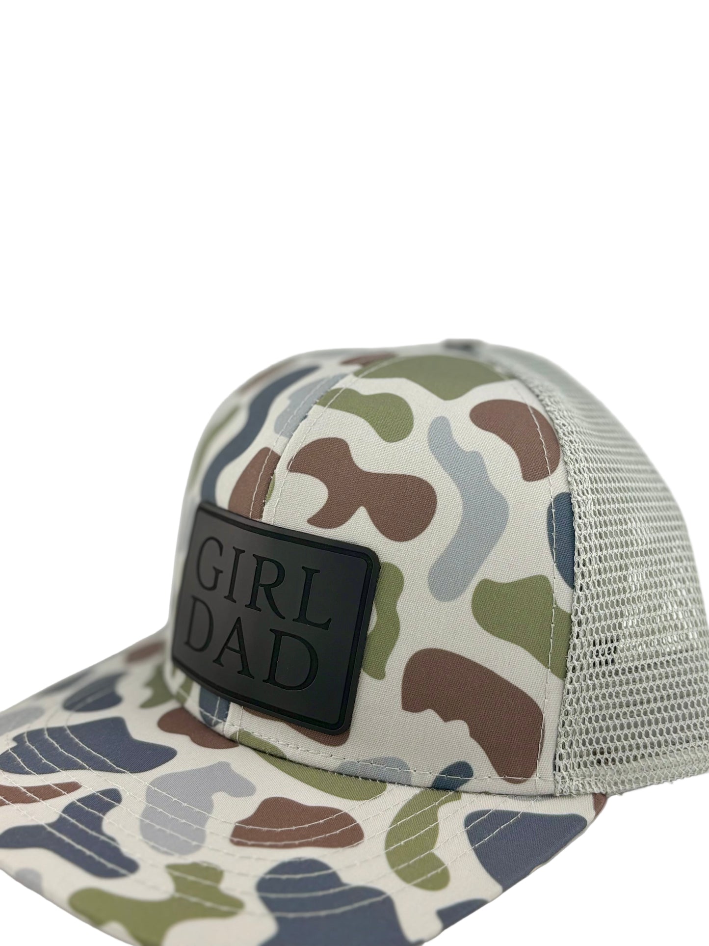 "Side view of a camo trucker hat with a light gray mesh back and structured front panel. The black rectangular patch showcases the embossed words 'GIRL DAD,' adding a sleek and rugged look for proud fathers."