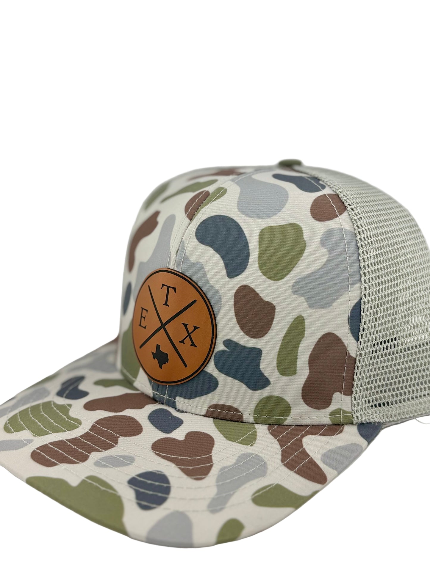 "Side view of a camo trucker hat with a light gray mesh back and a structured front panel. The brown leather patch features a crossed-line design with 'E,' 'T,' and 'X,' along with a Texas state silhouette, making it a stylish and regional statement piece."