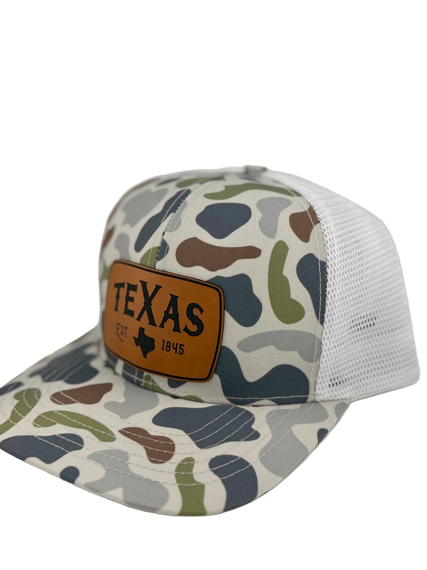 "Side view of a camo trucker hat with a white mesh back and a structured front panel. The brown leather patch displays 'TEXAS,' the state outline, and 'EST. 1845,' creating a rustic and outdoorsy look that celebrates Texas pride."