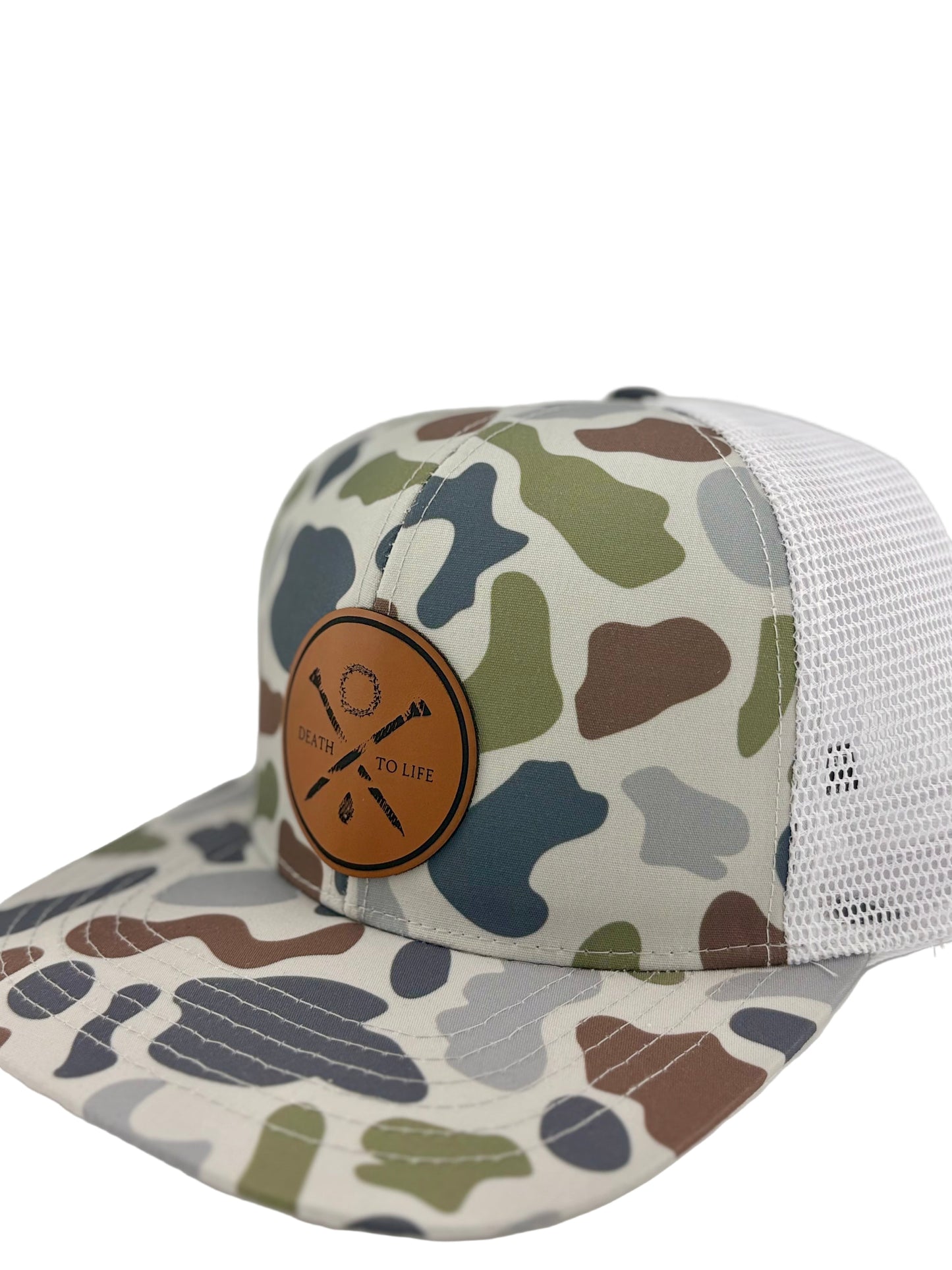 "Side view of a camo trucker hat with a structured front panel and a breathable white mesh back. The brown leather patch on the front showcases crossed arrows, a wreath, and the words 'Death to Life,' emphasizing a rugged yet stylish look."