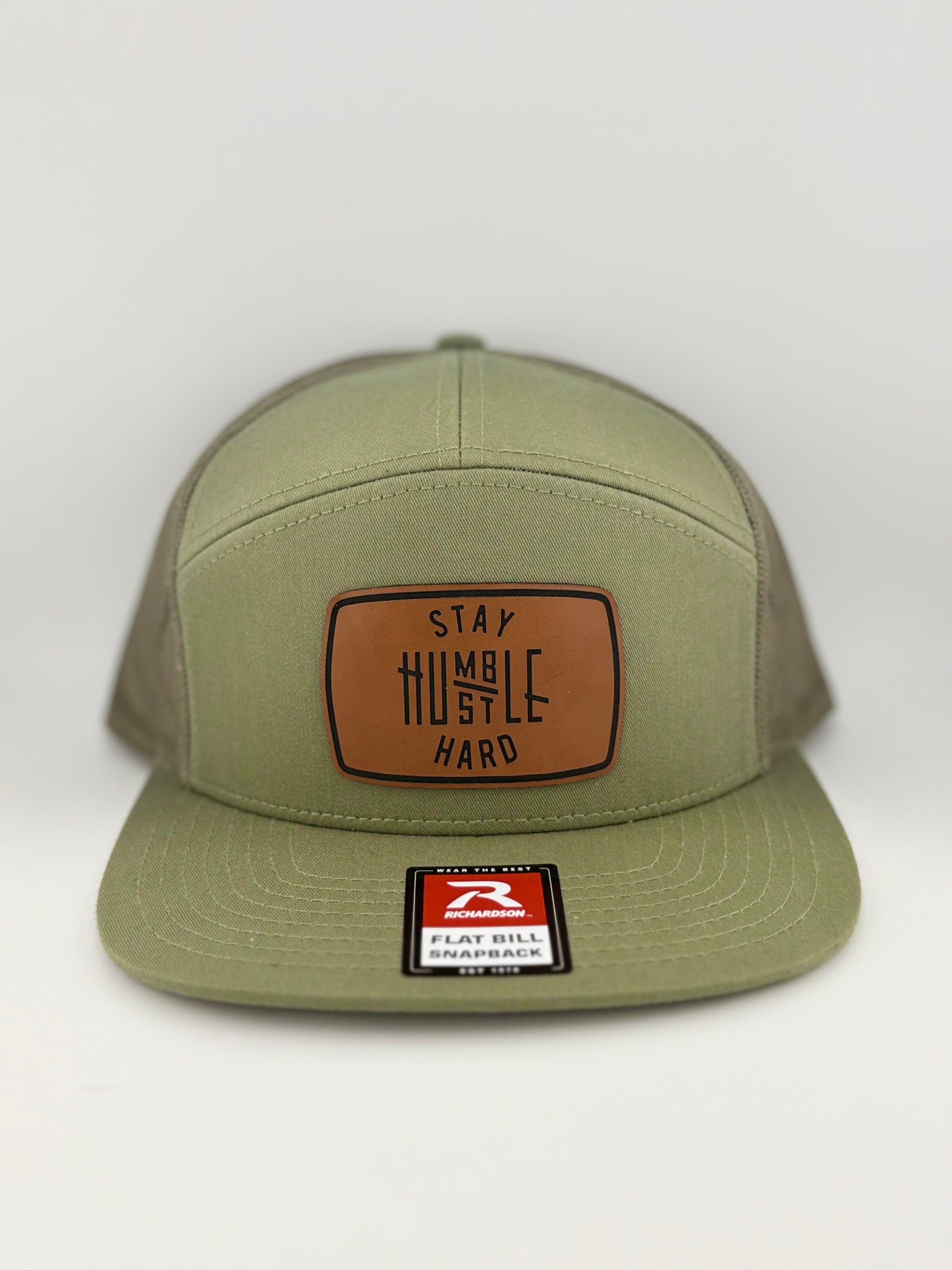 "Olive green Richardson 112 snapback hat with a leather patch that reads 'Stay Humble, Hustle Hard.' The hat features a structured front panel, mesh back, and a flat bill."