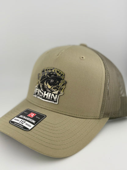 "Side view of a tan trucker hat with a tan mesh back and structured front panel. The front patch displays a bass fish in sunglasses with the phrase 'WISHIN' I WAS FISHIN',' making it a fun and stylish choice for anglers. A Richardson 112 label is visible on the brim."