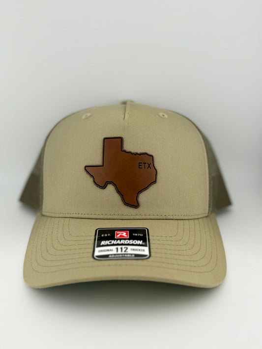 "Khaki-colored trucker hat with a structured front panel and a matching mesh back. A brown Texas-shaped patch is featured on the front, embossed with the letters 'ETX,' representing East Texas pride. A Richardson 112 label is affixed to the brim, indicating its adjustable fit."