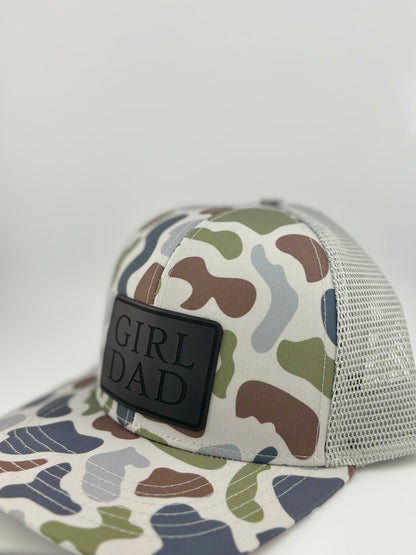 "Side view of a camo trucker hat with a light gray mesh back and structured front panel. The black rectangular patch showcases the embossed words 'GIRL DAD,' adding a sleek and rugged look for proud fathers."